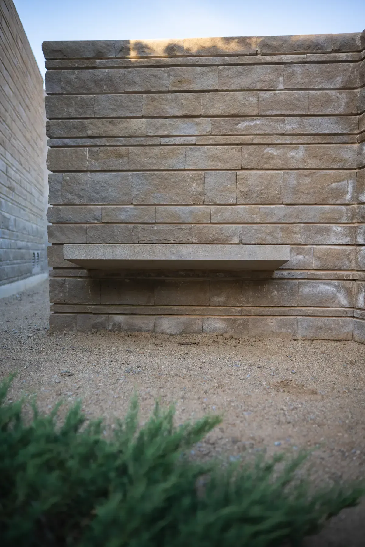 Banco de piedra integrado en el muro, con la pieza del asiento volada sobre el paño